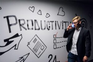 image of man on a cellphone walking in front of a whiteboard with the work "productivity" and other images to represent efficiency and thus lean concepts